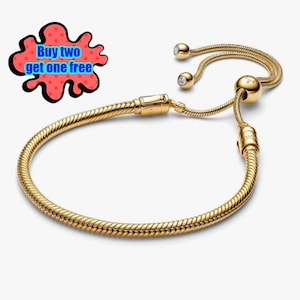 May include: A gold-coloured bracelet with a snake chain design. The bracelet has a sliding clasp and two small, clear gemstones. The text "Buy two get one free" is in a red and black bubble.