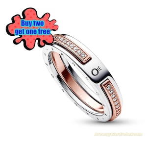 May include: A silver ring with rose gold accents and embedded clear stones. The ring has the word "PANDORA" engraved on the side. A red and blue graphic bubble with the text "Buy two get one free" is in the upper left corner.
