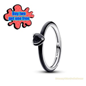 Puede incluir: Un anillo de plata con una banda de esmalte negro y una piedra negra en forma de corazón. El anillo tiene la palabra "PANDORA" grabada en el lateral. Un gráfico rojo y negro con el texto "Buy two get one free" en el fondo.
