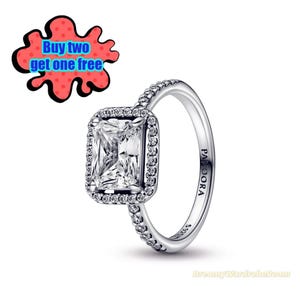 Pode incluir: Um anel prateado com uma pedra preciosa retangular e transparente no centro, rodeada por pedras menores e transparentes. A banda do anel também é adornada com pequenas pedras transparentes. A palavra "PANDORA" é visível na banda do anel. Um gráfico vermelho e preto diz "Buy two get one free".