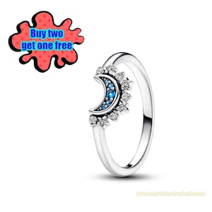 May include: A silver ring featuring a crescent moon design with blue gemstones and surrounding star accents. The ring has a delicate band and is set against a white background. The image also includes a red and blue promotional graphic that says "Buy two get one free."