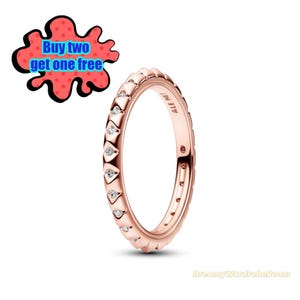 May include: Rose gold ring with a repeating pattern of teardrop-shaped designs, each set with a small, clear gemstone. The ring has the text "ALE MET" engraved on the side. A red and black graphic with the text "Buy two get one free" is in the background.