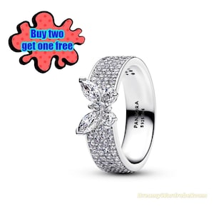 Peut inclure: Une bague en argent avec un motif floral. La bague présente un anneau recouvert de petites pierres transparentes et une pièce maîtresse en forme de fleur avec des pierres de taille marquise. La bague est marquée "PANDORA S925 ALE".