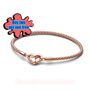 Peut inclure: Bracelet en or rose avec un fermoir en forme de cœur. Le bracelet présente un motif texturé et tissé. Le fermoir est gravé du nom de la marque "Pandora". Un graphique rouge et bleu avec le texte "Buy two get one free" est en haut à gauche.