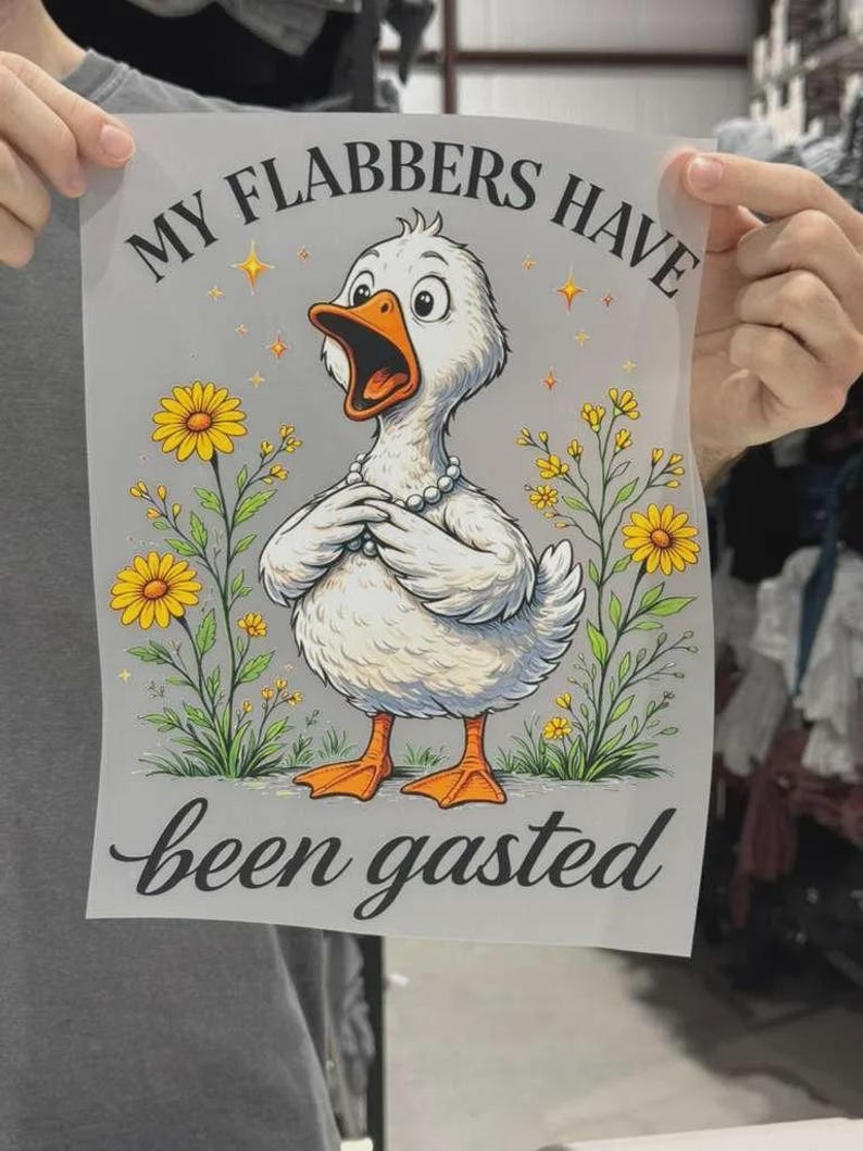 K&ouml;nnte beinhalten: Ein rechteckiger Druck mit einer wei&szlig;en Ente mit orangefarbenem Schnabel und F&uuml;&szlig;en, die eine Perlenkette tr&auml;gt. Die Ente ist von gelben Blumen und Sternchen umgeben. Der Text lautet oben MY FLABBERS HAVE und unten been gasted.