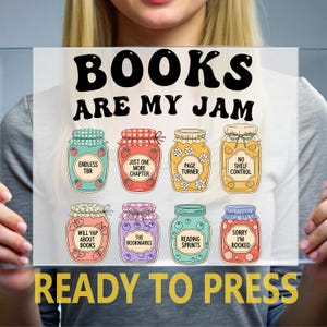 May include: A clear rectangular sign with the text "BOOKS ARE MY JAM" and "READY TO PRESS". Below the text are illustrations of eight jam jars with book-related phrases like "Endless TBR" and "Sorry I'm Booked".