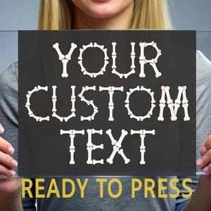 May include: A black rectangular sign with the words "YOUR CUSTOM TEXT" in white, bone-shaped letters. The phrase "READY TO PRESS" is in yellow at the bottom. The sign is held up by a person.