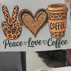 K&ouml;nnte beinhalten: Ein Grafik-Transferbogen mit einem Peace-Zeichen im Leopardenmuster, einem Herz mit goldener Glitzertextur und einem Kaffeebecher im Leopardenmuster. Darunter steht in schwarzer Schrift Peace, Love, and Coffee, getrennt durch kleine Herzen.