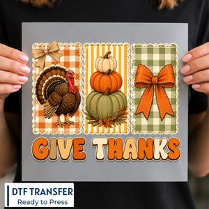 May include: A DTF transfer sheet featuring three rectangular panels with scalloped edges. The left panel shows a turkey on orange gingham, the centre shows stacked pumpkins on yellow stripes, and the right shows an orange bow on green gingham. The text GIVE THANKS appears below in orange.
