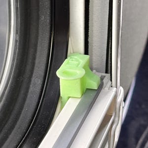 Puede incluir: Primer plano de un pestillo de ventana de plástico verde claro. El pestillo está instalado en un marco de ventana con componentes negros, blancos y grises. El pestillo tiene las letras "LP".