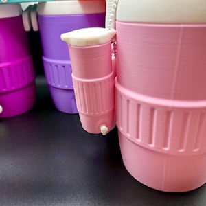 May include: A close-up of several colorful water bottles. The bottles are pink, purple, and magenta. Each bottle has a white lid and a small, attached cup. The bottles have a ribbed design around the middle and a small spout on the cup.