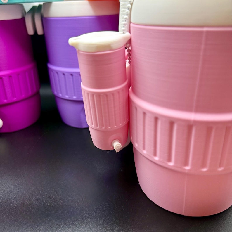 May include: A close-up of several colorful water bottles. The bottles are pink, purple, and magenta. Each bottle has a white lid and a small, attached cup. The bottles have a ribbed design around the middle and a small spout on the cup.