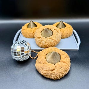 May include: Four brown, textured, donut-shaped objects with a bronze-colored cone in the center, arranged on a gray tray. A small disco ball with mirrored tiles hangs nearby. The background is black.