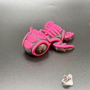 May include: A 3D-printed, black and pink decorative object with a rounded shape and a crystal-like gem. The object has a textured surface with pink accents. The gem is clear with a faceted design.