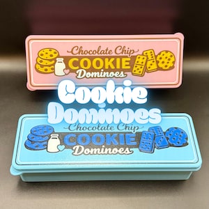 Puede incluir: Dos cajas rectangulares con las palabras "Cookie Dominoes". La caja superior es rosa con ilustraciones de galletas y domin&oacute;s, y el texto "Chocolate Chip". La caja inferior es azul con ilustraciones y texto similares.