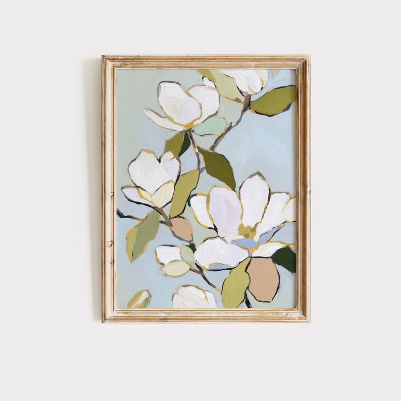 Puede incluir: Una impresi&oacute;n art&iacute;stica enmarcada que presenta flores de magnolia blancas con detalles dorados y hojas verdes sobre un fondo azul claro. La obra de arte est&aacute; enmarcada en madera dorada, creando una est&eacute;tica cl&aacute;sica.