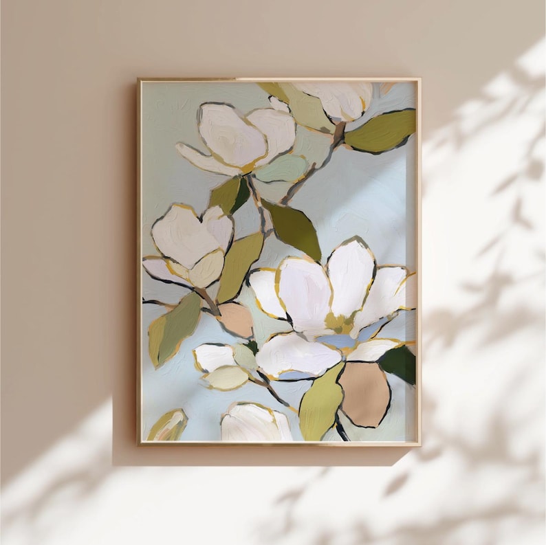 Puede incluir: Impresi&oacute;n art&iacute;stica enmarcada que representa flores de magnolia blancas con detalles dorados y hojas verdes sobre un fondo azul claro. La obra de arte se presenta en un marco de madera delgado y claro, ofreciendo una est&eacute;tica contempor&aacute;nea y refinada.