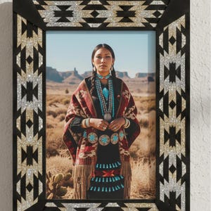 May include: A framed photograph featuring a woman in traditional Native American attire. The frame is black with a geometric pattern in silver and gold glitter. The woman is wearing a patterned shawl, turquoise jewelry, and a black dress.