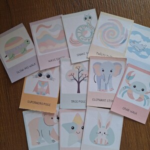 May include: A set of 12 colorful cards featuring different animal poses and actions. Each card has a cute illustration of an animal, such as a turtle, snake, elephant, crab, bear, and bunny, and a corresponding action phrase, such as "Slow-Mo Walk", "Wave Dance", "Snake Slide", "Superhero Pose", "Tree Pose", "Elephant Stomp", "Crab Walk", "Bear Walk", "Star Jump", and "Bunny Hops".