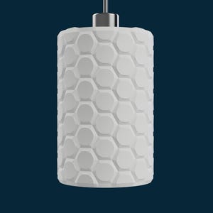 May include: A white cylindrical pendant light with a honeycomb pattern. The light fixture is suspended from a silver-colored metal fixture against a dark blue background. The honeycomb pattern is made up of hexagonal shapes.