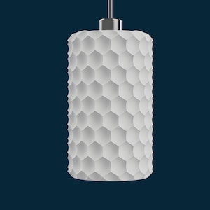 May include: A white, cylindrical pendant light fixture with a honeycomb pattern. The light hangs from a silver-colored metal fixture against a dark blue background. The shade is made of a series of hexagonal shapes.