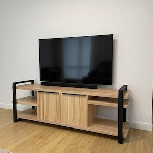 May include: A light wood entertainment center with black metal accents and two doors. The entertainment center has three shelves and is sitting on a wood floor.