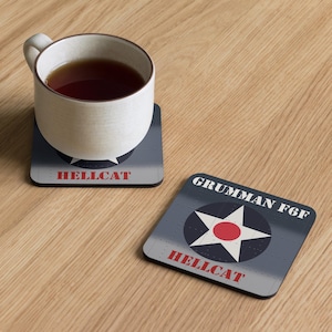 May include: Two square coasters with a Grumman F6F Hellcat design. One coaster has a white star with a red center, the text "HELLCAT" in red, and the text "GRUMMAN F6F" in white. A white mug with tea sits on one coaster.