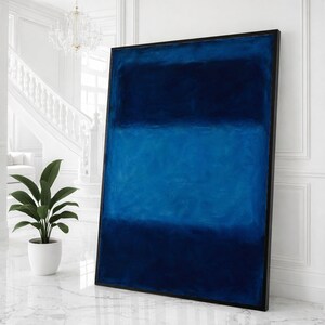 Puede incluir: Gran pintura abstracta enmarcada en tonos azules. La obra de arte se divide en tres bandas horizontales de diferentes tonos, desde el azul marino oscuro hasta el azul claro. La pintura se exhibe en una habitación luminosa y blanca.