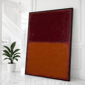 May include: Large abstract painting with a black frame. The artwork features two horizontal color blocks: a deep burgundy at the top and a vibrant orange at the bottom. The painting is displayed against a white wall.