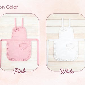 Pode incluir: S&atilde;o apresentados dois aventais, um rosa e outro branco. Cada avental tem uma borda com babados, um patch em forma de cora&ccedil;&atilde;o e um la&ccedil;o na parte superior. O texto "Apron Color" est&aacute; no topo, e "Pink" e "White" est&atilde;o escritos abaixo.
