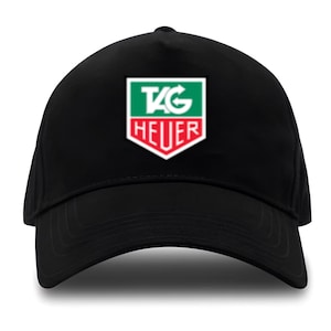 Può includere: Cappellino da baseball nero con visiera curva. Il cappellino presenta un logo con la scritta "TAG HEUER" in bianco, rosso e verde. Il logo è centrato sulla parte anteriore del cappellino.