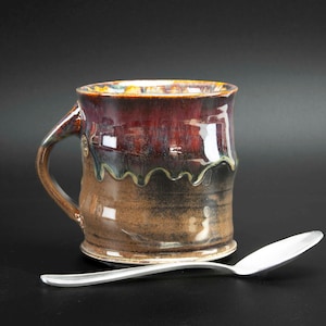 May include: A handmade ceramic mug with a brown, black, and red glaze. The mug has a unique, wavy design and a handle.