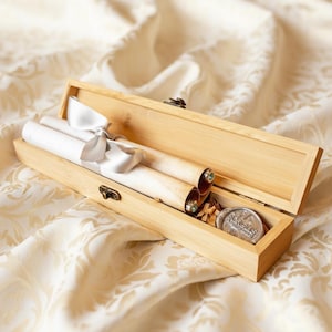 May include: A light-colored wooden box with a hinged lid, containing rolled scrolls tied with a white ribbon. The box also holds a wax seal. The scrolls are made of parchment-like paper.