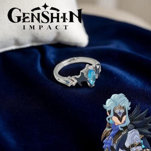 May include: Silver ring with a light blue gemstone and detailed design. The ring features dark blue accents and small blue gems. The words "Genshin Impact" are printed in black above the ring.