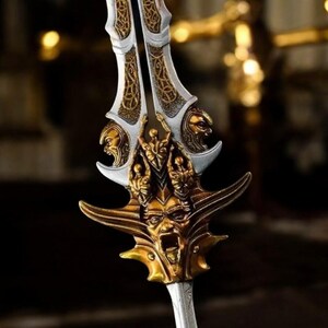 May include: A detailed close-up of a decorative sword with a silver blade and ornate gold accents. The hilt features multiple sculpted faces and intricate patterns, creating a fantasy or historical aesthetic.