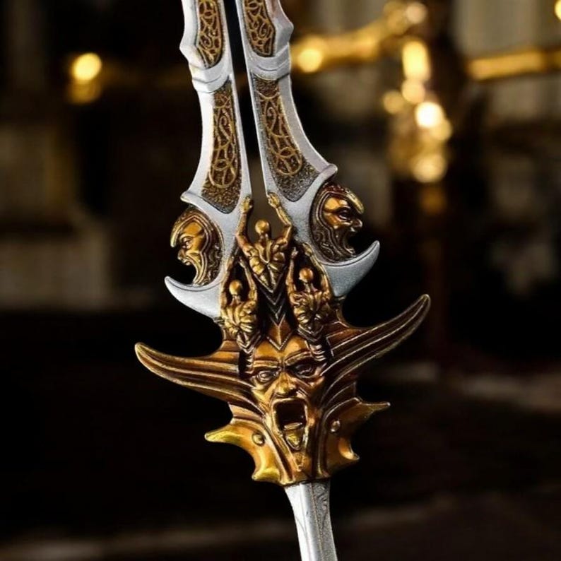 May include: A detailed close-up of a decorative sword with a silver blade and ornate gold accents. The hilt features multiple sculpted faces and intricate patterns, creating a fantasy or historical aesthetic.