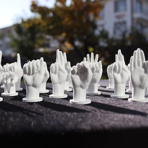 May include: A collection of white, 3D printed hands in various poses, arranged in a row on a black surface.