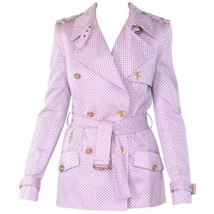 May include: A light purple trench coat with a polka dot pattern. The double-breasted coat features gold-colored buttons, a belt, and pockets. The coat has long sleeves and a classic trench coat design.