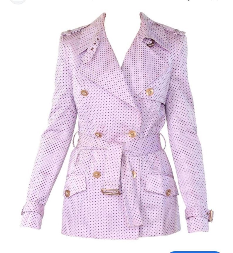May include: A light purple trench coat with a polka dot pattern. The double-breasted coat features gold-colored buttons, a belt, and pockets. The coat has long sleeves and a classic trench coat design.