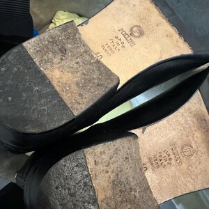 May include: Black leather shoes with worn soles. The soles are marked "POLLINI MADE IN ITALY VERO CUOIO 40". The shoes are likely Italian-made, with a focus on quality and craftsmanship.
