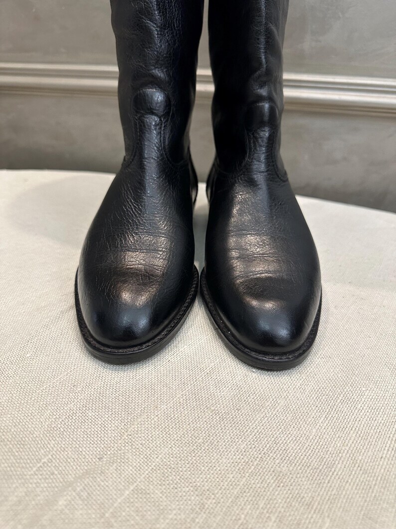 May include: A pair of black leather boots. The boots have a classic design with a rounded toe and a mid-calf height. The leather has a textured appearance, and the boots appear to be unworn.