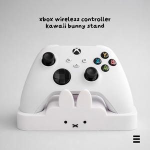 Könnte beinhalten: Ein weißer Xbox Wireless Controller auf einem weißen Hasenständer. Der Controller hat schwarze Joysticks und farbige Knöpfe. Der Ständer hat ein Hasengesicht mit schwarzen Punkten und einem Kreuz. Der Text 'xbox wireless controller kawaii bunny stand' ist oben.