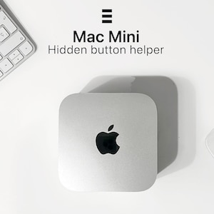 Może przedstawiać: Srebrny komputer Mac Mini z logo Apple, umieszczony na białej powierzchni. Tekst "Mac Mini Hidden button helper" jest wyświetlany nad komputerem. Biała klawiatura jest częściowo widoczna w lewym górnym rogu.