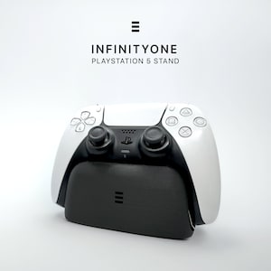 Könnte beinhalten: Ein weiß-schwarzer PlayStation 5-Controller auf einem schwarzen Ständer. Auf dem Ständer steht der Text "INFINITYONE PLAYSTATION 5 STAND". Der Controller hat ein symmetrisches Design mit verschiedenen Tasten und Joysticks.