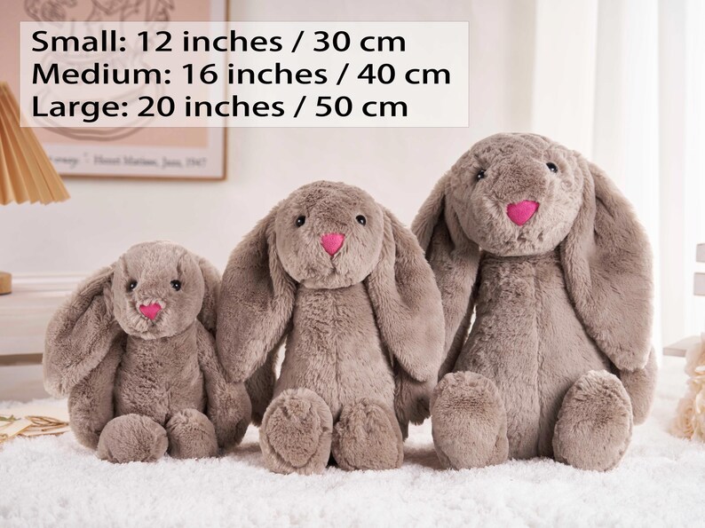 May include: Three plush bunny rabbits in varying sizes. The smallest is 12 inches, the medium is 16 inches, and the largest is 20 inches. Each bunny is gray with a pink nose. The text on the image reads: Small: 12 inches / 30 cm, Medium: 16 inches / 40 cm, Large: 20 inches / 50 cm.
