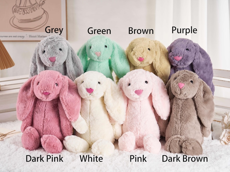 May include: A collection of plush bunny rabbits in various colors, including grey, green, brown, purple, dark pink, white, pink, and dark brown. Each bunny has long floppy ears, a pink nose, and a soft, cuddly appearance. The image includes text labels for each color.