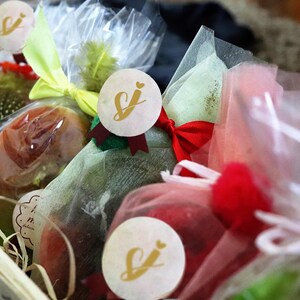 May include: A wooden basket containing wrapped gifts. The gifts are in clear cellophane, with colourful ribbons and decorative stickers. The stickers have a gold logo. The gifts are in various colours, including red, green, and yellow.