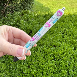 May include: A pen with a white glittery barrel featuring pink and blue dental-themed graphics. The pen has a black tip and a silver metal top. The design includes tooth, toothbrush, and dental tool illustrations.