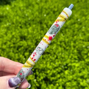 May include: A white pen with a crime scene theme. The pen features a fingerprint, blood splatters, handcuffs, and yellow "POLICE LINE" tape. The pen is held against a backdrop of green foliage.