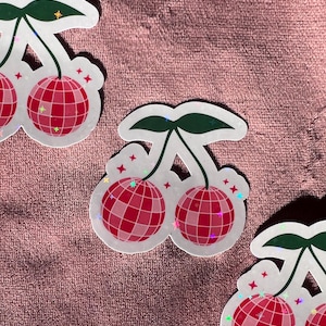 Op de afbeelding: Drie gestanste stickers met een paar kersen waarbij het fruit is afgebeeld als roze en rode discoballen met een rasterpatroon. Elke sticker heeft twee donkergroene bladeren aan de bovenkant en kleine rode steraccenten rondom.